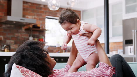 Mutter-Liegt-Auf-Dem-Sofa-Und-Hebt-Ihre-Kleine-Tochter-In-Die-Luft