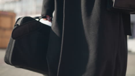 close-up of leather boot and stylish coat detail, showing a leg in sheer tights, exuding elegance and sophistication on an urban street with blurred background featuring building and bikes