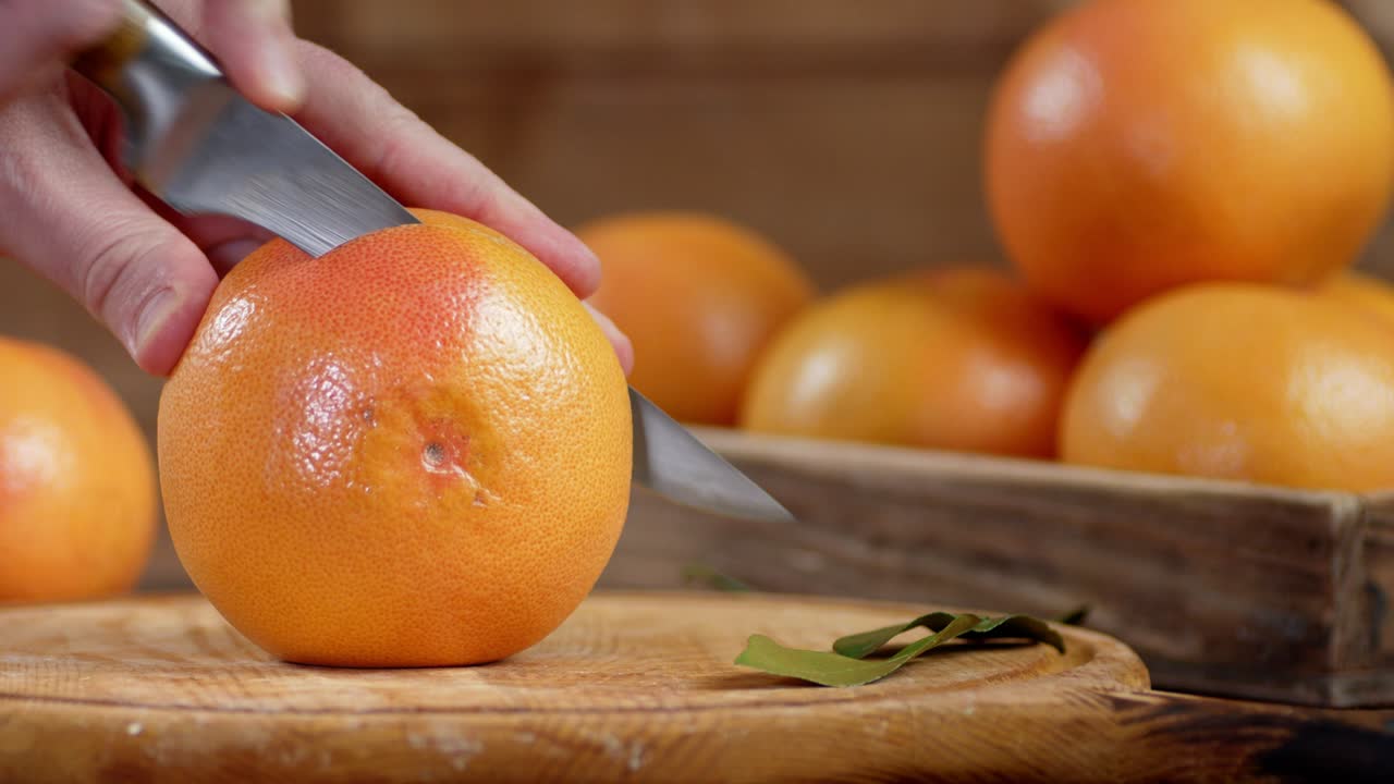 칼을 들고 있는 남성의 손은 그레이프프루트를 조각으로 잘라습니다.