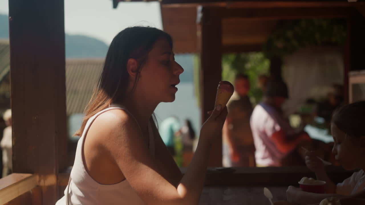 젊은 여성은 카페에서 딸과 함께 웨이퍼 코너에서 맛있는 아이스크림을 먹습니다. 레스토랑에서 작은 소녀와 함께 차가운 디저트를 신선하게합니다.