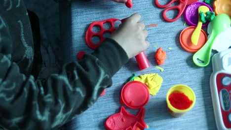 young boy playing with colorful non-toxic putty dough plasticine cutting out holes with tube and other acessories