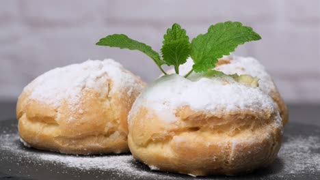 baked custard eclairs and sprinkled with powdered sugar and decorated with a mint leaf on a black board