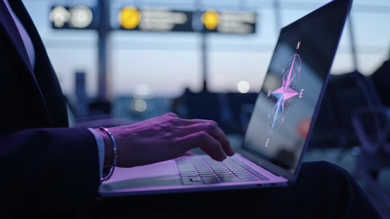 A Business Traveler Engaged in Work at an Airport, Utilizing a Laptop with a Compass Graphic While Awaiting Their Next Journey in the Late Evening.