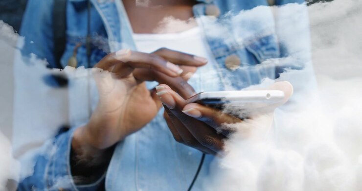 Femme tapotant son smartphone dans un environnement technologique et initiant des couches de nuages dérivantes enveloppant l'écran et la veste.
