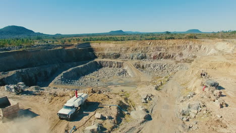 truck-driving-into-dusty-stone-quarry-gravel-pit,-wide-aerial-establishment-shot