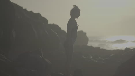 woman in silhouette at sunrise/sunset on rocky coast