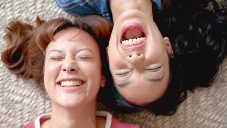 two young biracial female friends are lying down, heads together, sharing a joyful moment