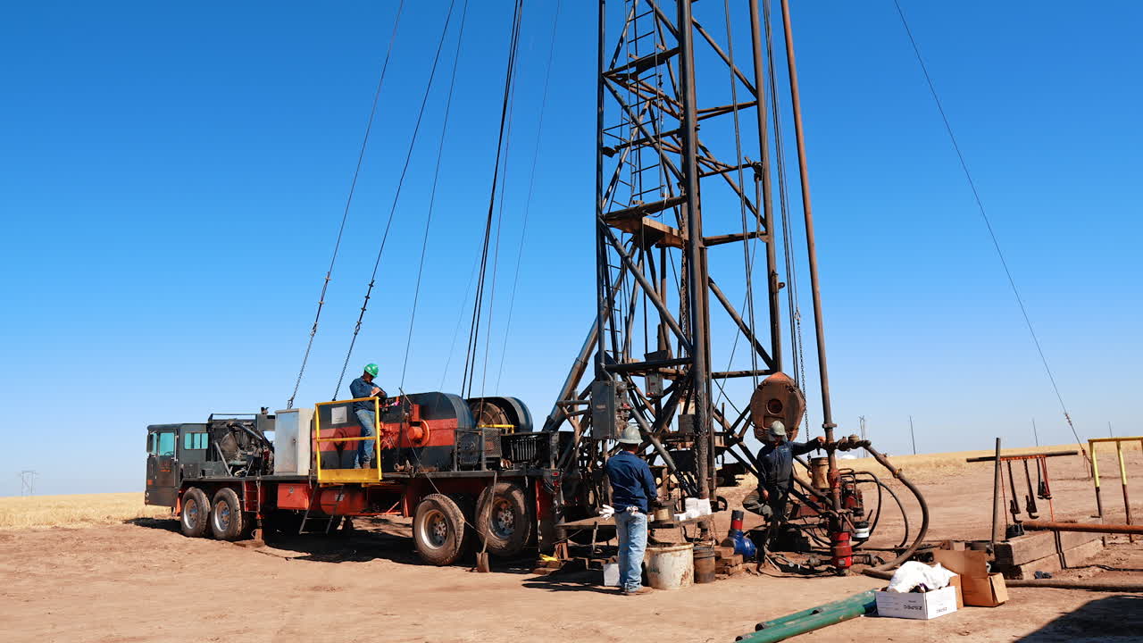 Two worker stand at the large truck with crane on top. Men produce oil or gas in the deserted area.