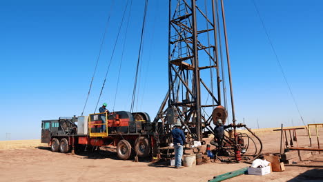 two worker stand at the large truck with crane on top. men produce oil or gas in the deserted area.