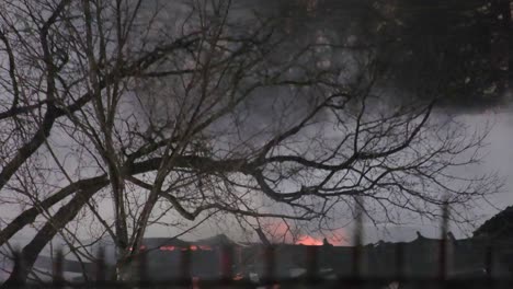 Un-Disparo-Distante-De-Agua-Rociada-Por-Los-Bomberos-Sobre-Las-Llamas-De-Un-Incendio-Residencial-Mientras-Una-Nube-De-Humo-Negro-Se-Eleva-Hacia-El-Cielo-Nocturno