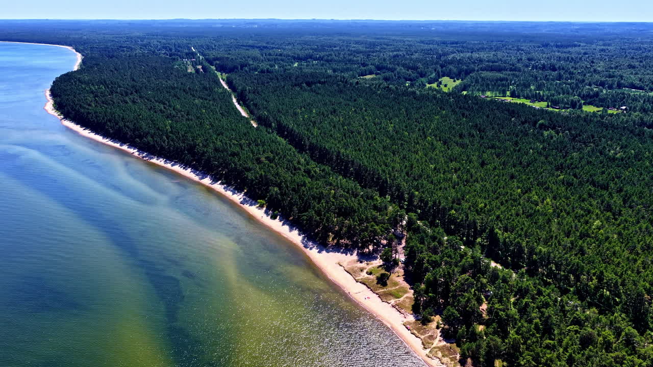 A spectacular aerial panning shot reveals the vast and unspoiled natural beauty of the Engure coastline in Latvia, where a dense pine forest meets a serene sandy beach along the Baltic Sea