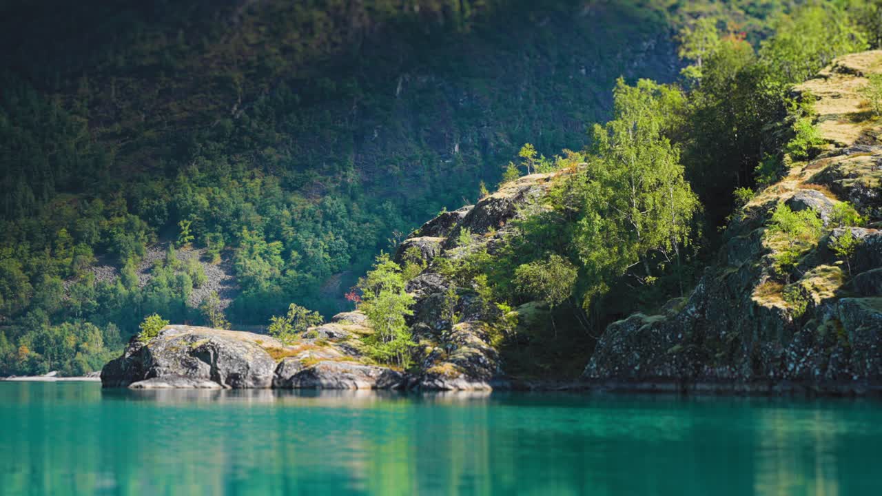 화려한 풍경, 바위가 있는 해안과 에메랄드색 물, 숲으로 인 산, 밝은 빛으로 목욕하는 평온한 호수의 풍경.