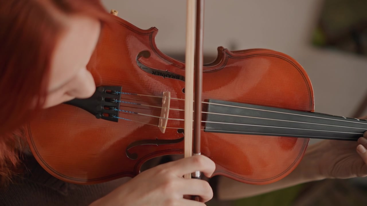 Closeup violin practice redhead student bowing in cozy music room, focused hands on fingerboard and chinrest, wooden instrument warmed by sunlight, careful bow stroke guided by teacher offcamera