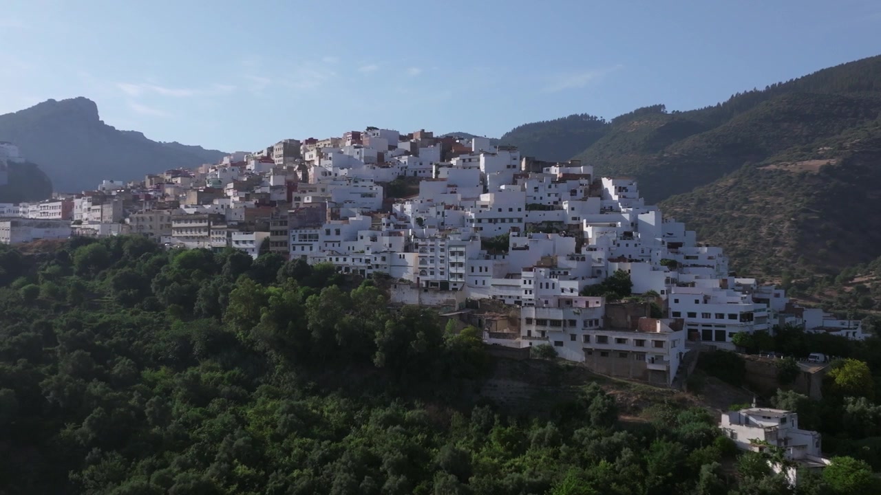 Veduta aerea con drone di Moulay Idriss Zerhoun, la storica città bianca collinare del Marocco settentrionale, circondata da una vegetazione lussureggiante e incorniciata dai Monti Zerhoun in un suggestivo paesaggio naturale