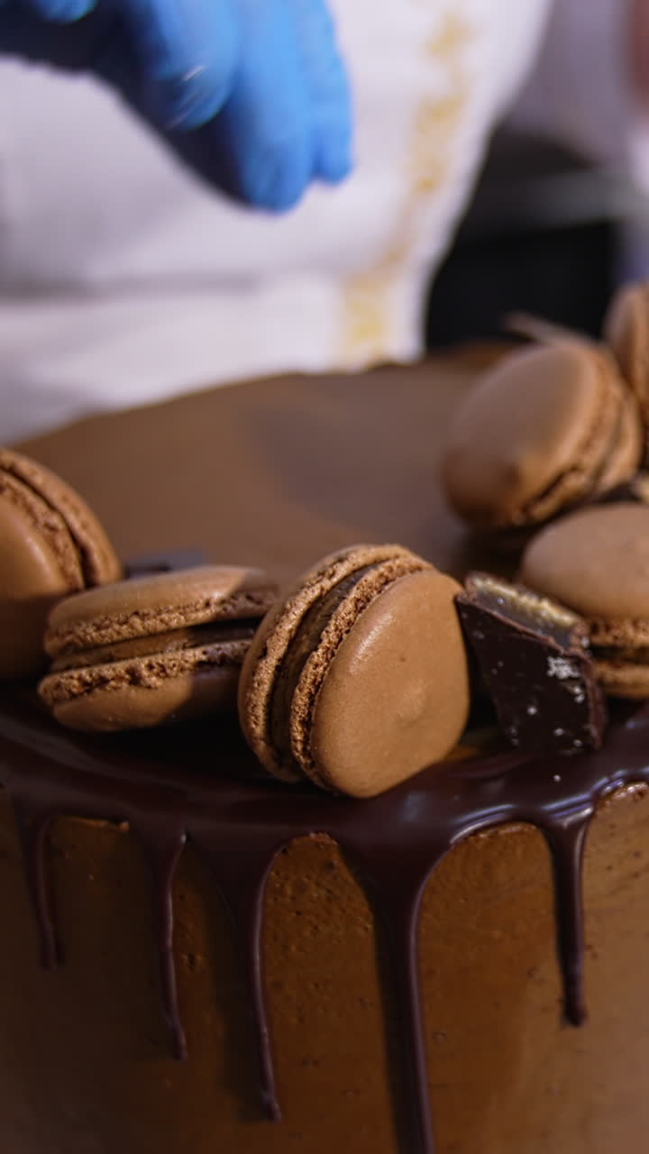 Tasty chocolate cake beautifully decorated in the food factory. Pastry professionals put the sweets on top of the big cake. Close up. Vertical video