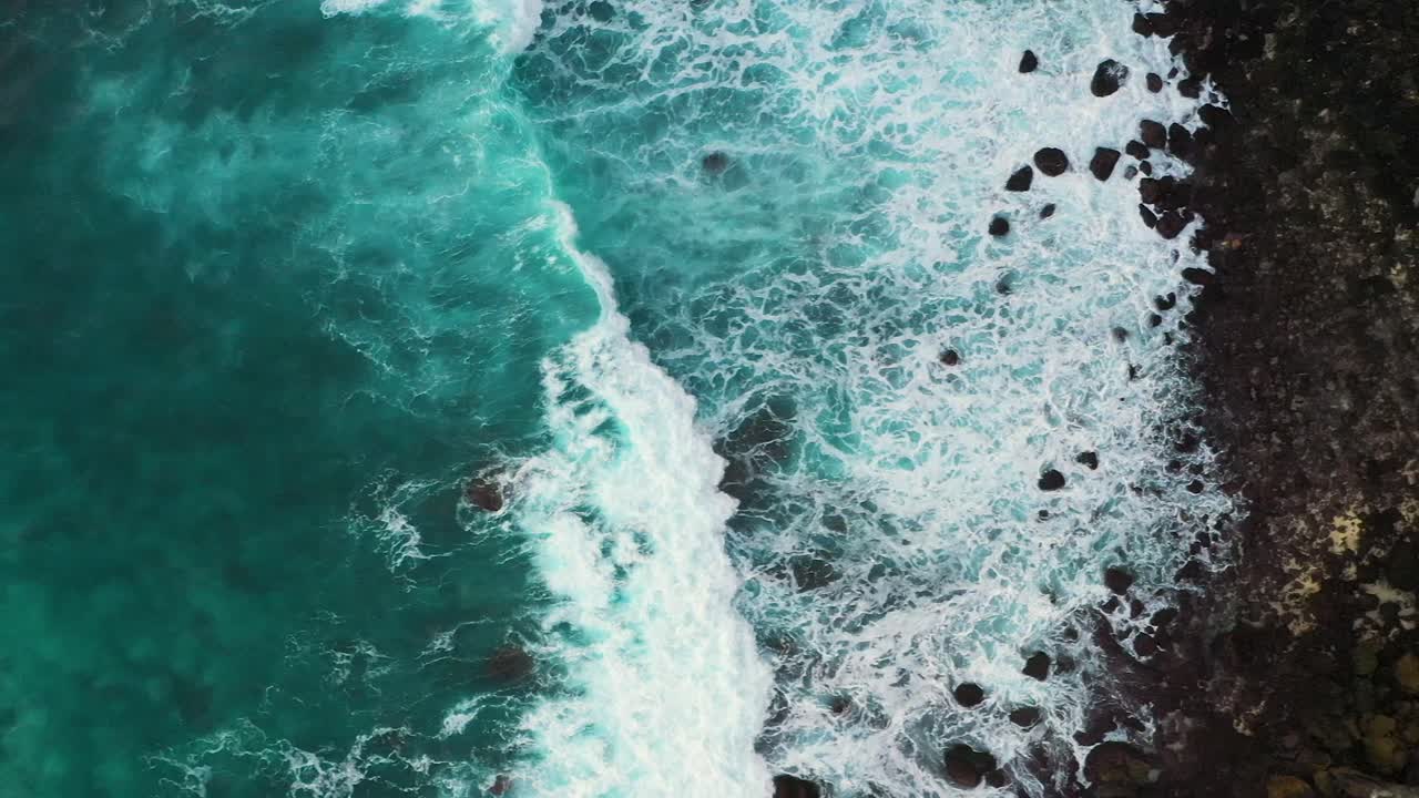 Letecký snímek tyrkysových oceánských vln narážejících na pobřeží s černým pískem ostrova Nusa Penida, jedné z turistických atrakcí ostrova Bali: Crystal Beach, Kelingking Beach, Angel Billabong, Broken Beach