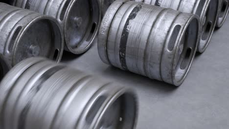 multiple metal beer kegs rolled on the ground sequential. a camera moves back in an endless, seamless loop. soft light illuminates surfaces of cold, steel, worn barrels. warehouse storage work.