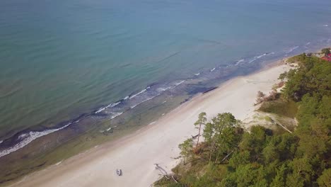 vista aérea de pájaro de la costa del mar báltico en un día soleado, dunas de arena blanca a la orilla del mar dañadas por las olas, bosque de pinos, erosión costera, cambios climáticos, disparos de drones de gran angular que avanzan-1