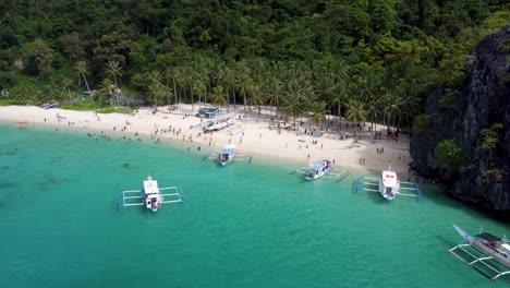 Seven-Commandos-Palm-Beach-In-El-Nido-Mit-Touristen-Auf-Weißem-Sand,-Die-Im-Blauen-Wasser-Schwimmen,-Und-Ausleger-Tourbooten,-Die-Sich-Im-Vordergrund-Bewegen