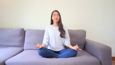 Hermosa-Mujer-Sentada-Con-Las-Piernas-Cruzadas-En-El-Sofá-Practicando-Yoga-En-Casa