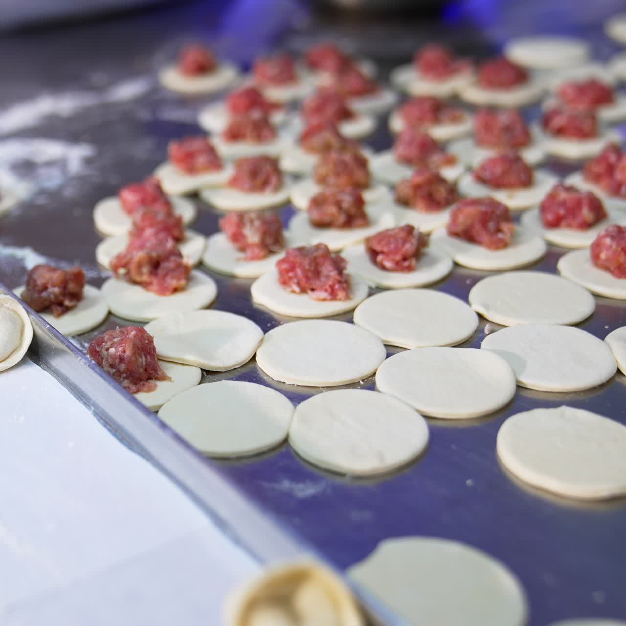 Little white dough circles are filled with minced meat. Semi-finished ravioli on the metal table in the cooking process. Close up