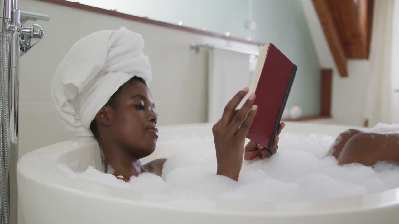 Profile of african american attractive woman relaxing in bath and reading book in bathroom
