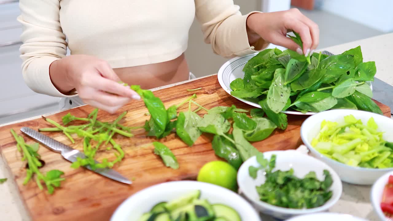 Hands preparing fresh basil on a wooden board in a bright kitchen. Natural lighting enhances the vibrant green colors