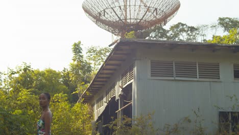 a sexy girl in a long dress walks at an abandoned military base and tracking station in the background