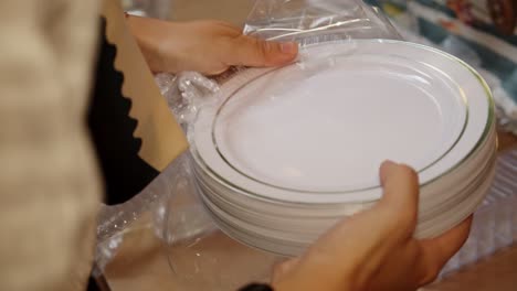 close up on woman's hands unwrapping plastic plates package for catering for outdoor social event in the evening