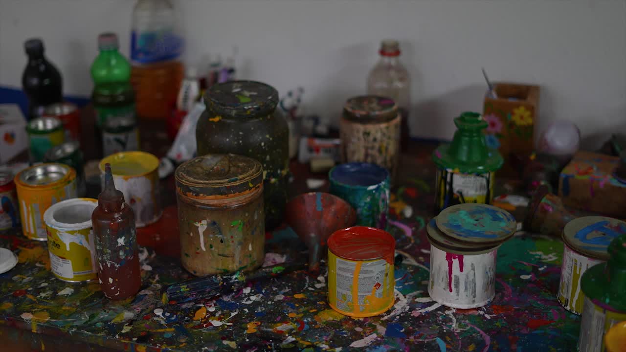 Messy artist's workbench with colorful paint cans and splatters