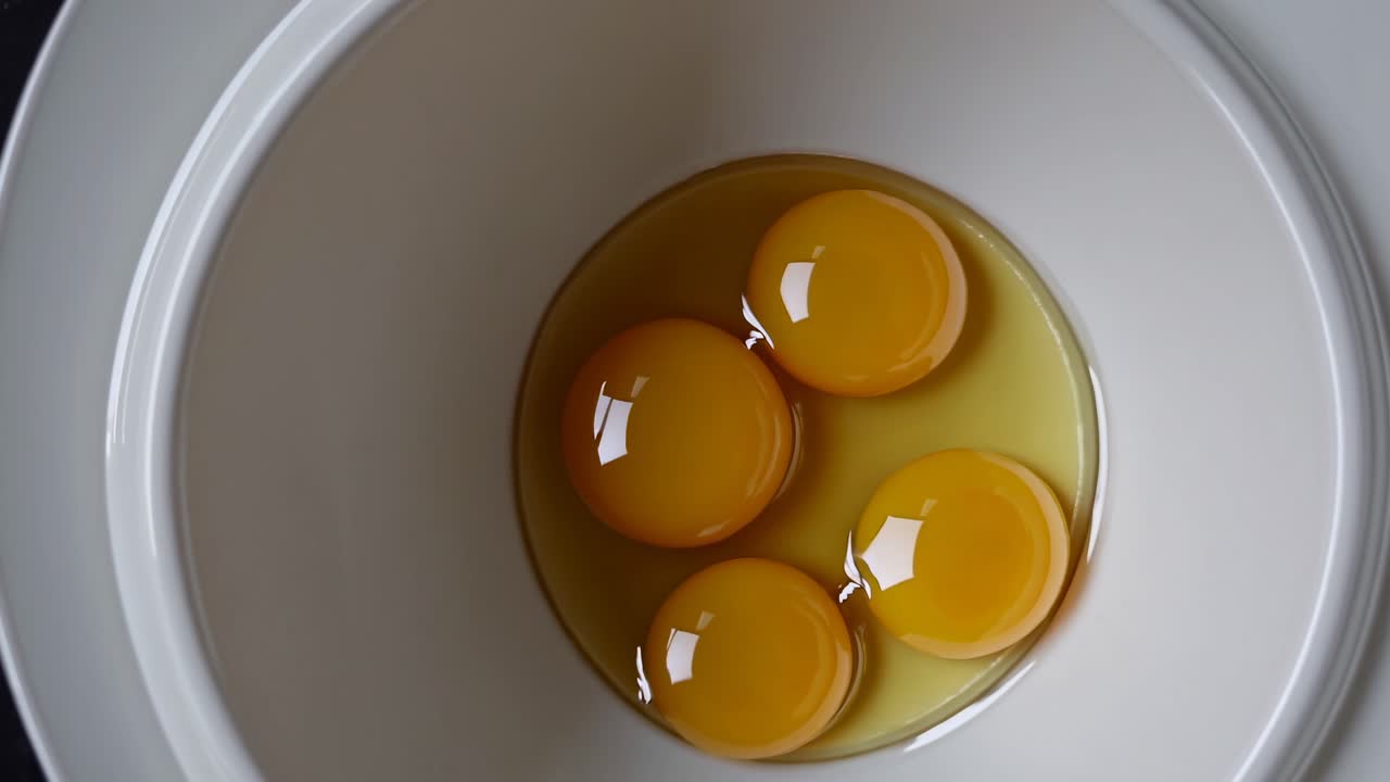 Top-down video shot of four egg yolks in a white bowl, emphasizing simplicity and culinary