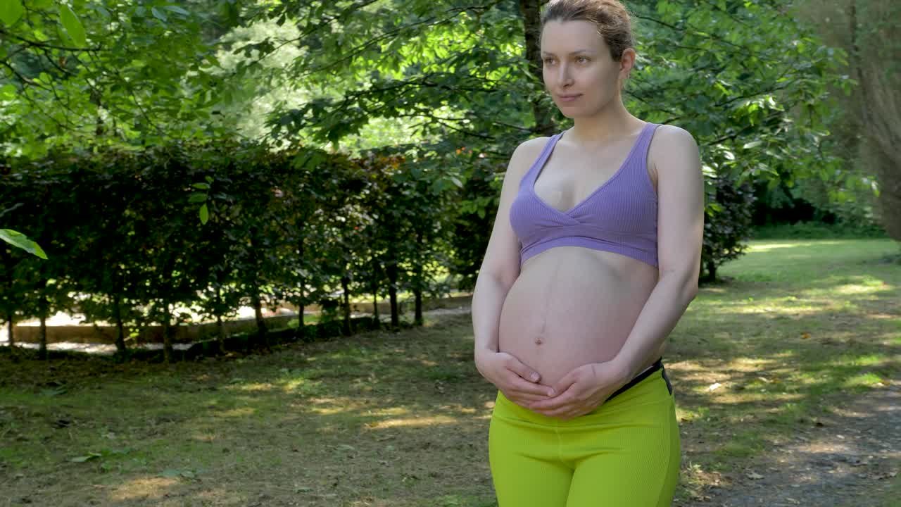 Donna incinta che si tiene la pancia mentre passeggia in giardino