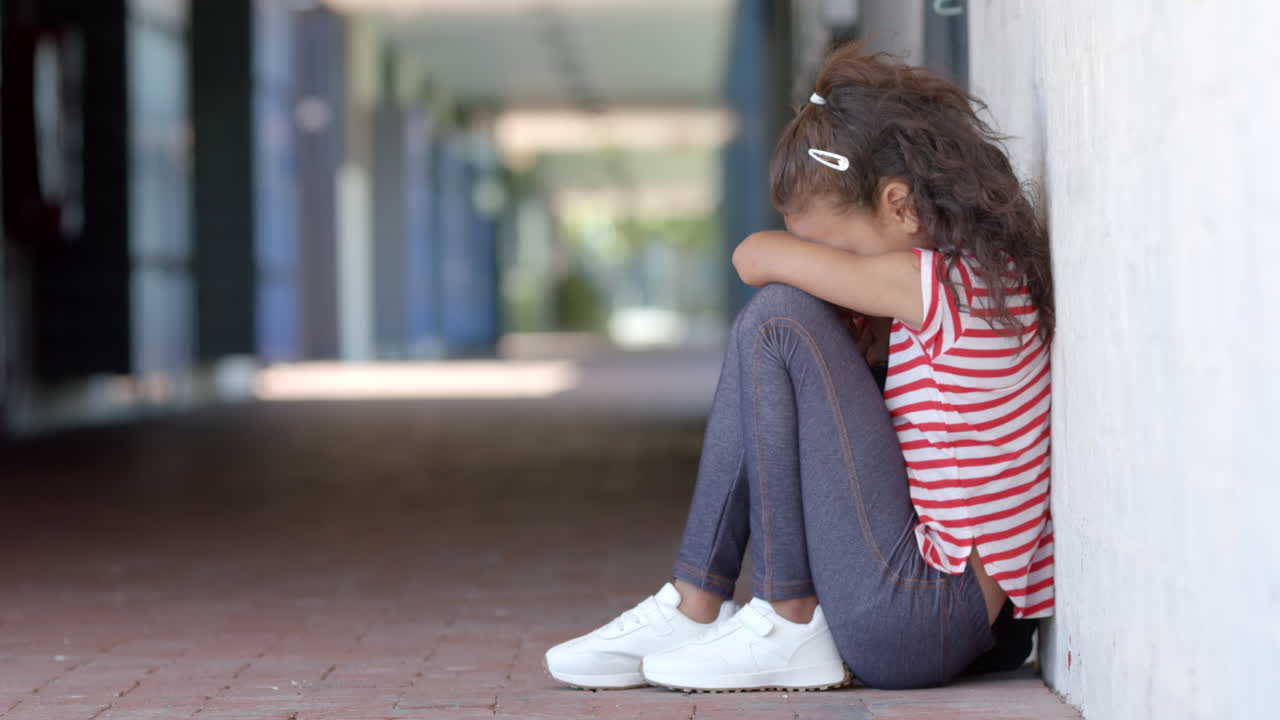 In school, child sitting alone against wall, feeling sad and upset, copy space