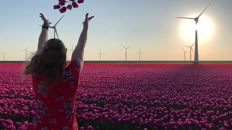 girl in field of tulips and wind turbines throwing flowers in air, slow motion