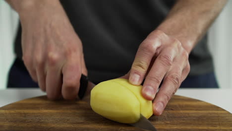 person cutting potato wedges on chopping board at home, closeup