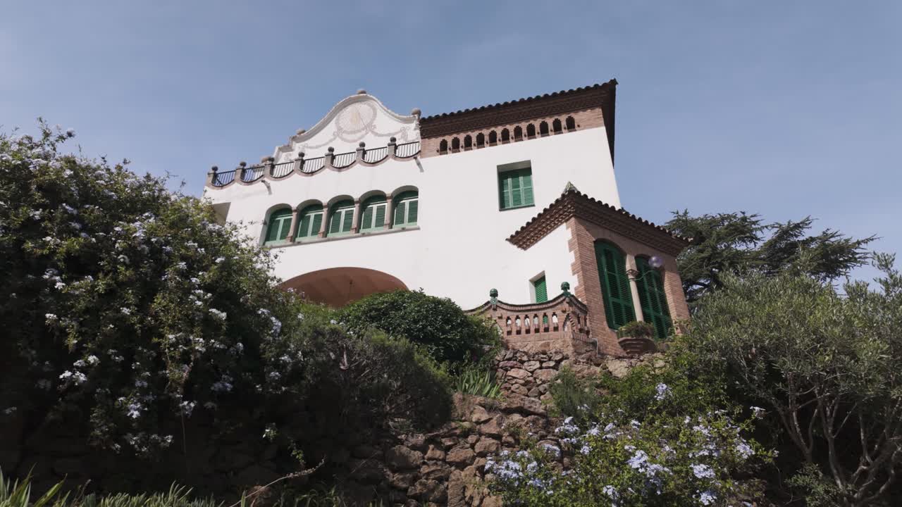 A charming view of Park Güell's Casa Trias with vibrant greenery and rustic stonework, Barcelona