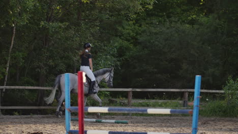 Professional-girl-rider-galloping-on-a-horse.-Girl-riding-a-horse-on-an-arena-at-sunset.-Horse-hoof-creates-a-lot-of-dust.-Competitive-rider-training-jumping.