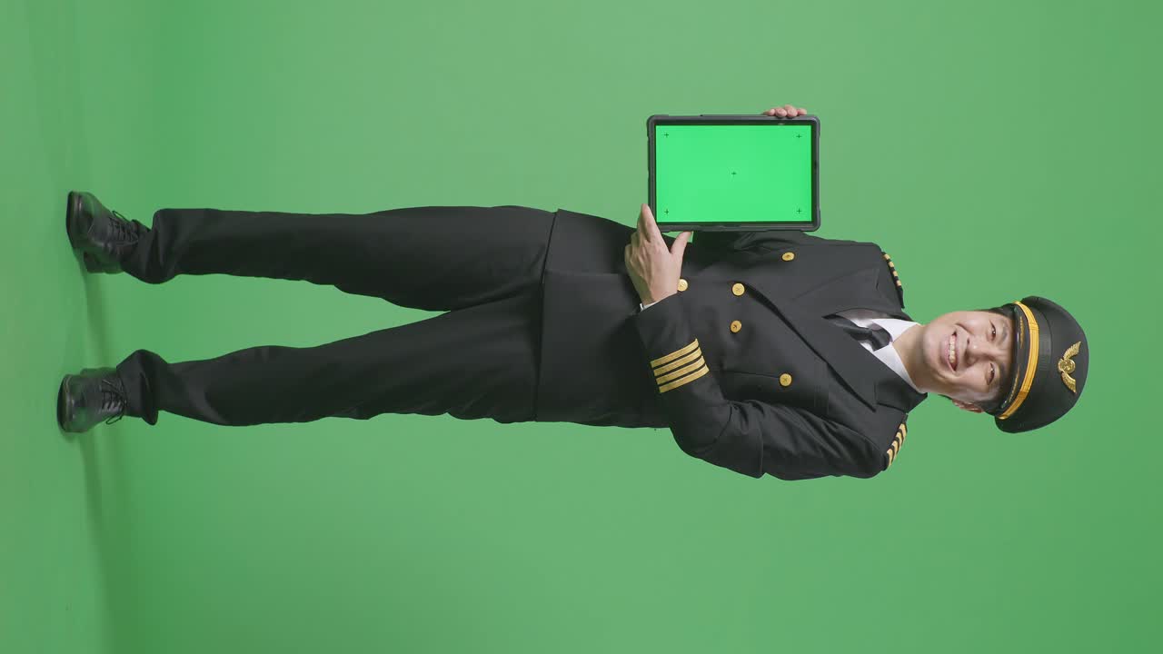 Full Body Of Asian Man Pilot Smiling And Showing Green Screen Tablet To The Camera While Standing In The Green Screen Background Studio
