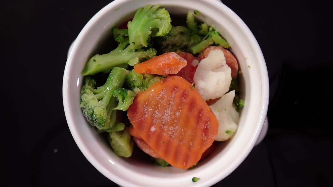 Primo piano dall'alto di verdure al vapore che ruotano in una ciotola, tra cui broccoli, carote e cavolfiore