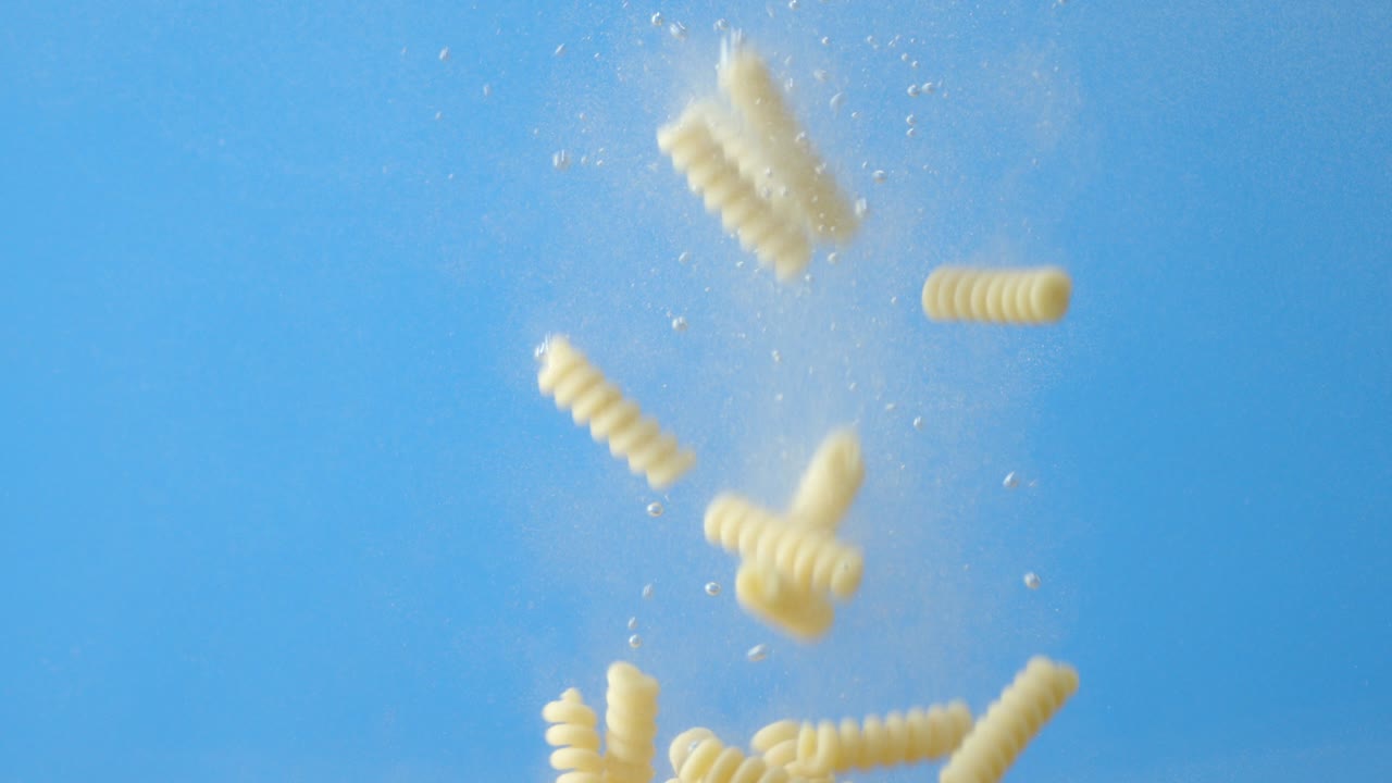 fusilli de pasta seca cayendo bajo el agua con burbujas de aire.
