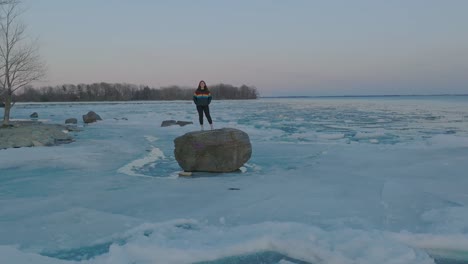 young-women-wearing-pride-colors-jacket-on-a-Rock-in-the-middle-of-a-frozen-lake