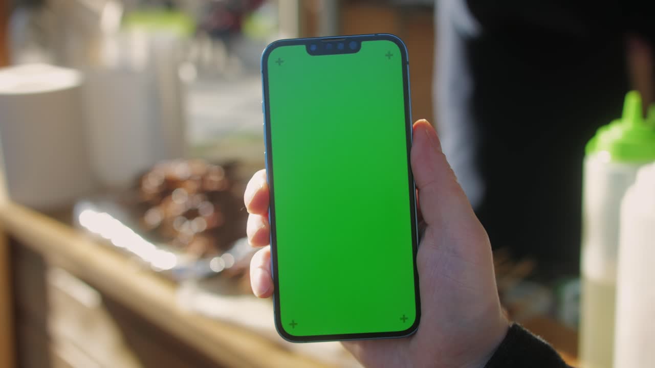 Young man holding phone chroma key screen on the street in front of food market close-up. Male with green screen on smart phone swiping .