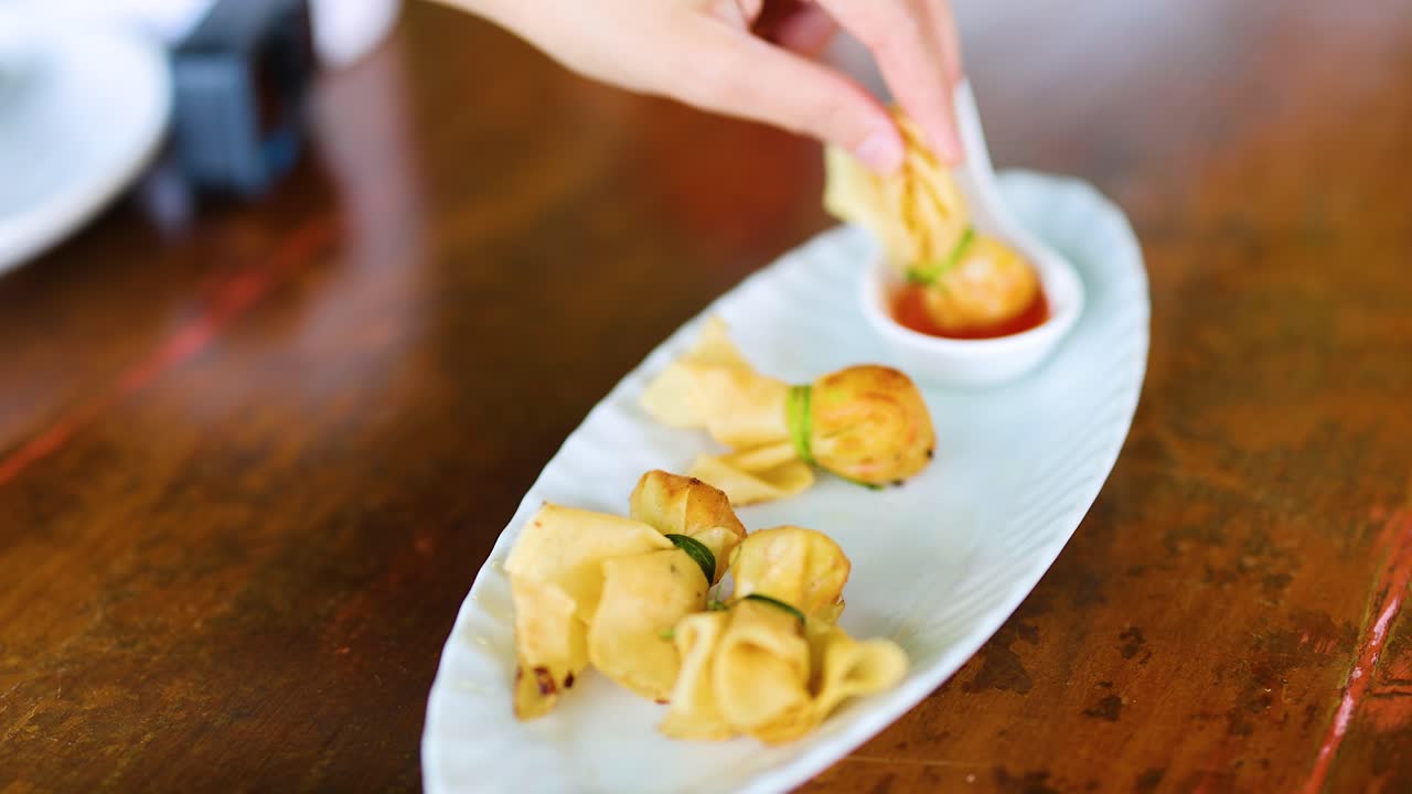 una mano recoge y sumerge albóndigas fritas en salsa en una mesa de madera a la luz natural
