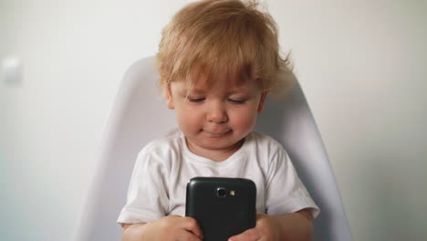 smiling boy in white t-shirt talks on cell phone on chair