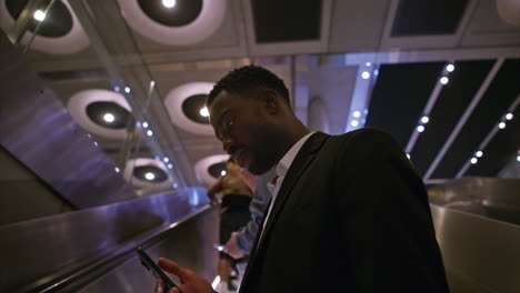 young businessman wearing suit commuting to work riding escalator at london underground station using mobile phone shot in real time