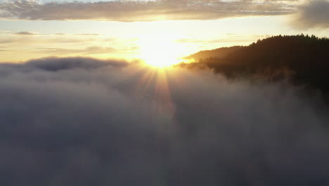 aerial drone footage of sunrays peaking over magical fog and mountain tops at sunset