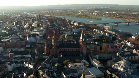 Perfekter-Drohnenkreis-Rund-Um-Den-Roten-Dom-Der-Biontech-Stadt-Mainz-Mit-Dem-Rhein-Im-Hintergrund