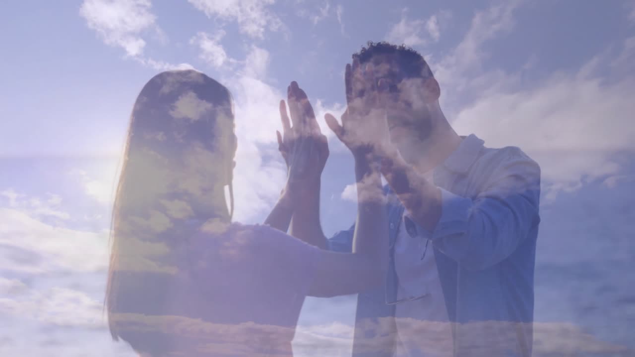 Pareja levantando las manos en la orilla, iniciando un ritmo de palmadas, mostrando una superposición de nube para un anuncio de tecnología.