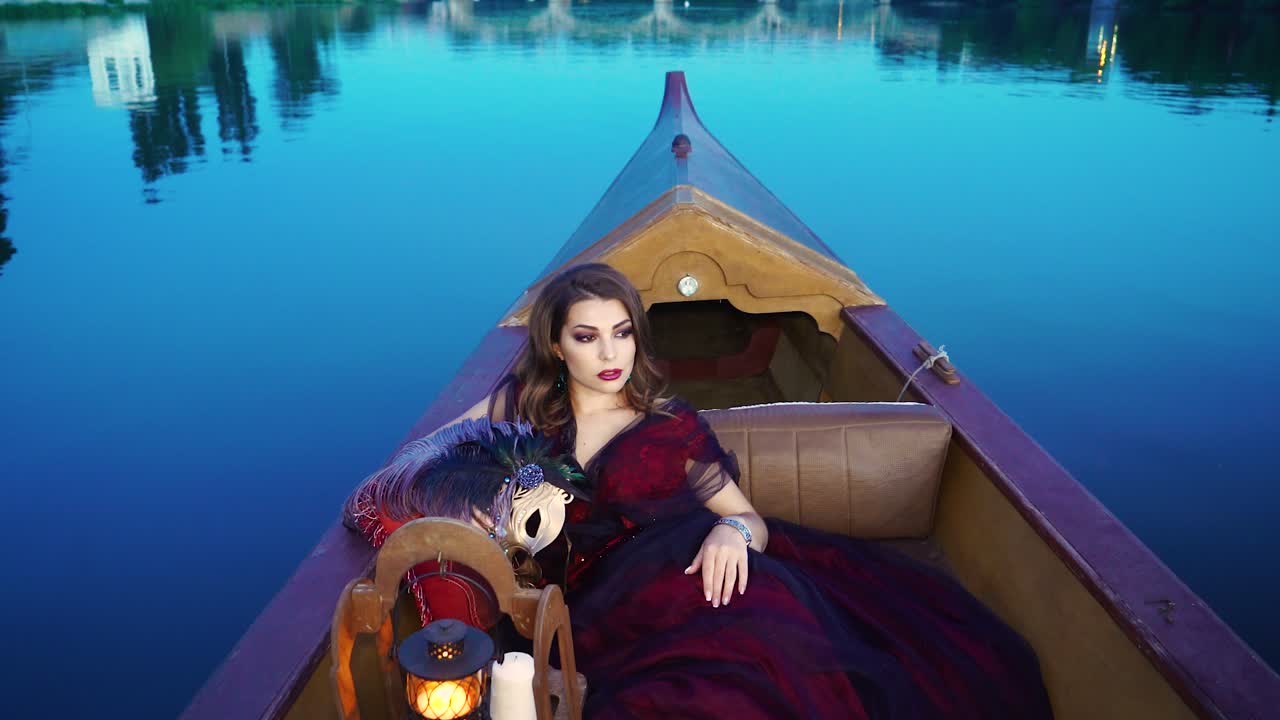 A charming woman in a red dress is riding in the gondola in the evening. Carnival in Venice. Blue background