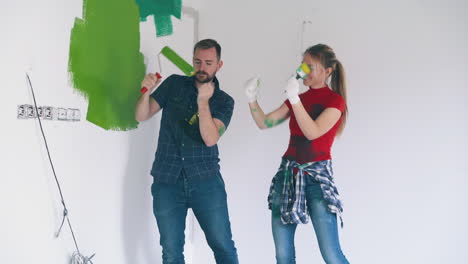 joyful-guy-and-girl-with-painting-tools-dance-in-room